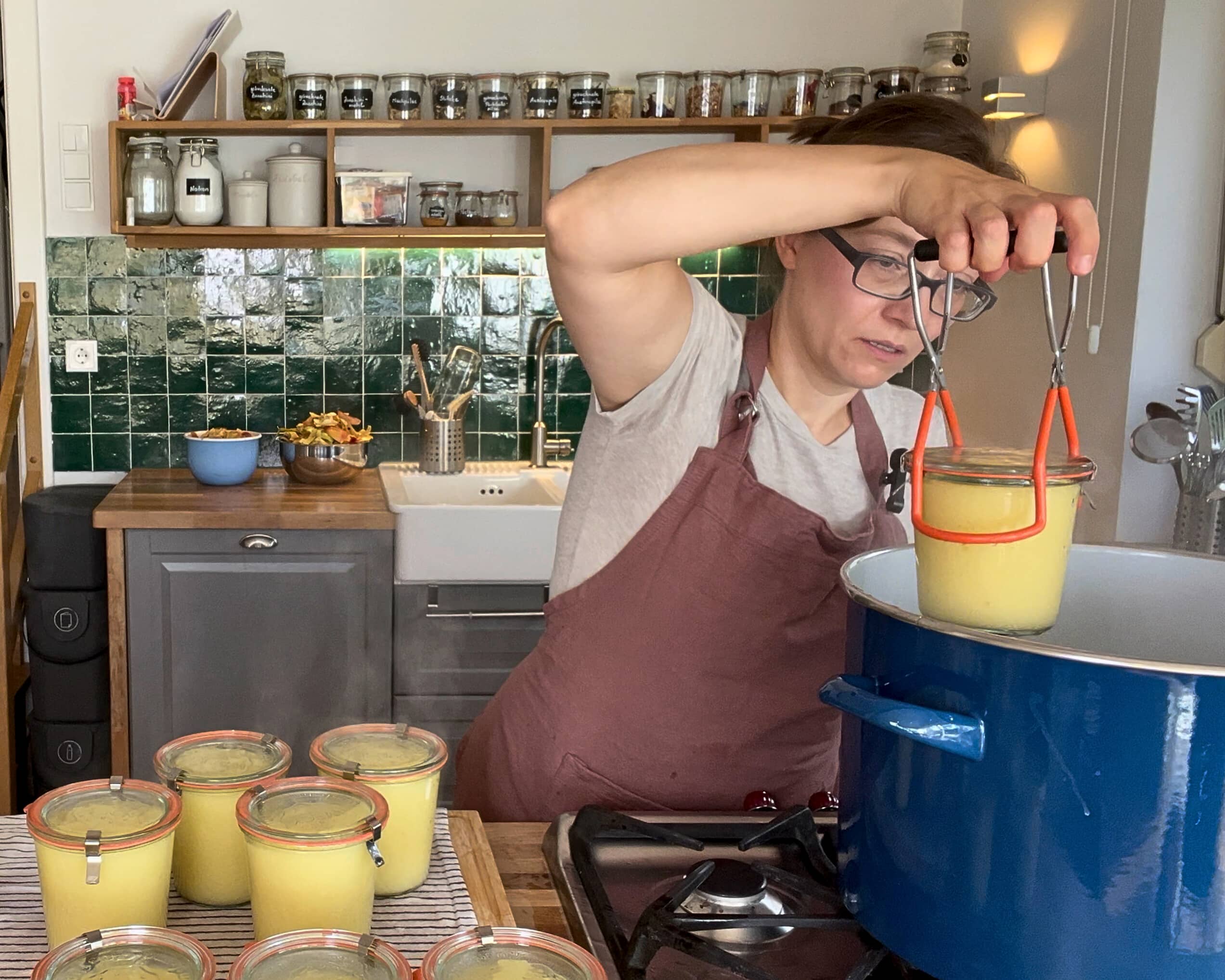 Einkochglas wird mit Glasheber aus dem kochenden Wasserbad herausgehoben