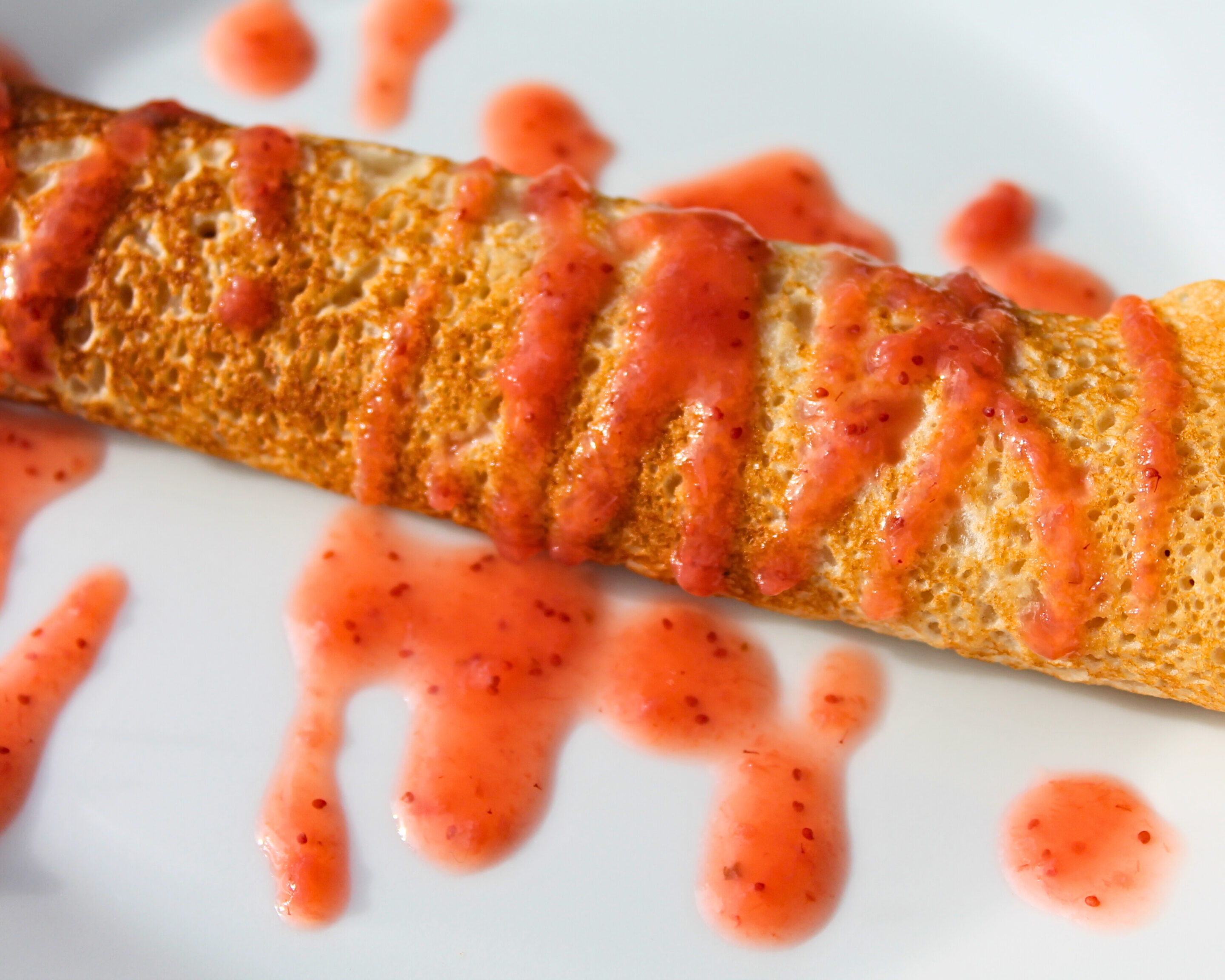 Vegane Pfannkuchen mit selbstgemachter Erdbeersauce, angerichtet auf einem weißen Teller – die Sauce ist über den Pfannkuchen geträufelt und bildet dekorative Tropfen auf dem Teller.