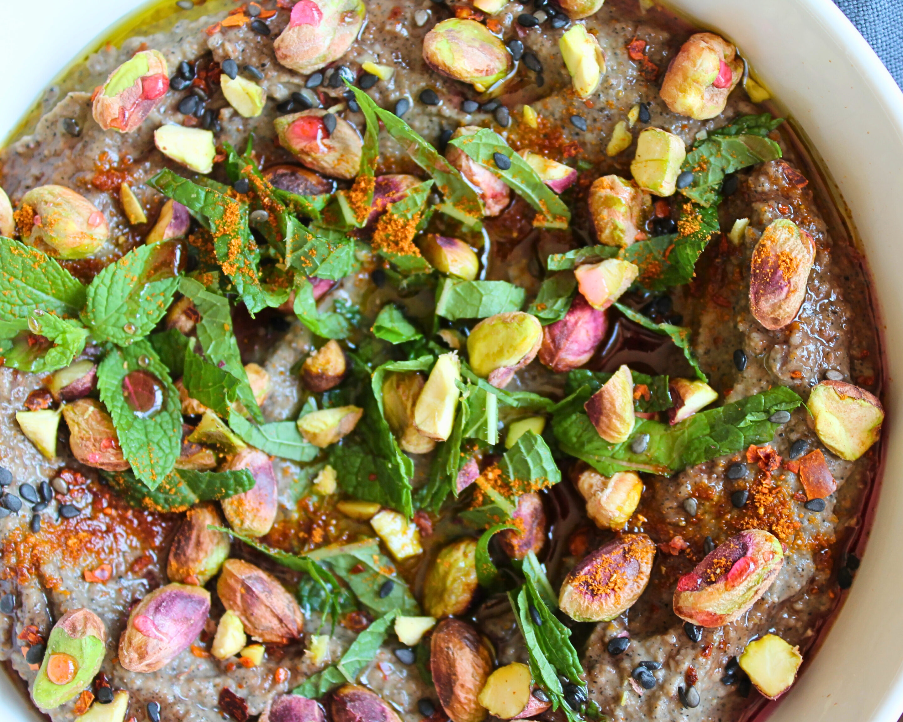 hummus-schwarze-kichererbsen-pistazien.jpg Dunkler Hummus aus schwarzen Kichererbsen, getoppt mit Pistazien, Minze, schwarzem Sesam und Chiliöl – Draufsicht
