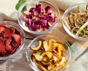 Getrocknete Zutaten für DIY-Rhabarbertee: Rosenblätter, Erdbeeren, Apfel und Rhabarber in Glasschalen