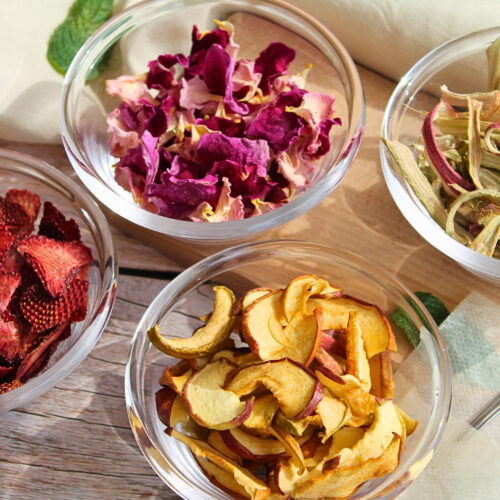 Getrocknete Zutaten für DIY-Rhabarbertee: Rosenblätter, Erdbeeren, Apfel und Rhabarber in Glasschalen