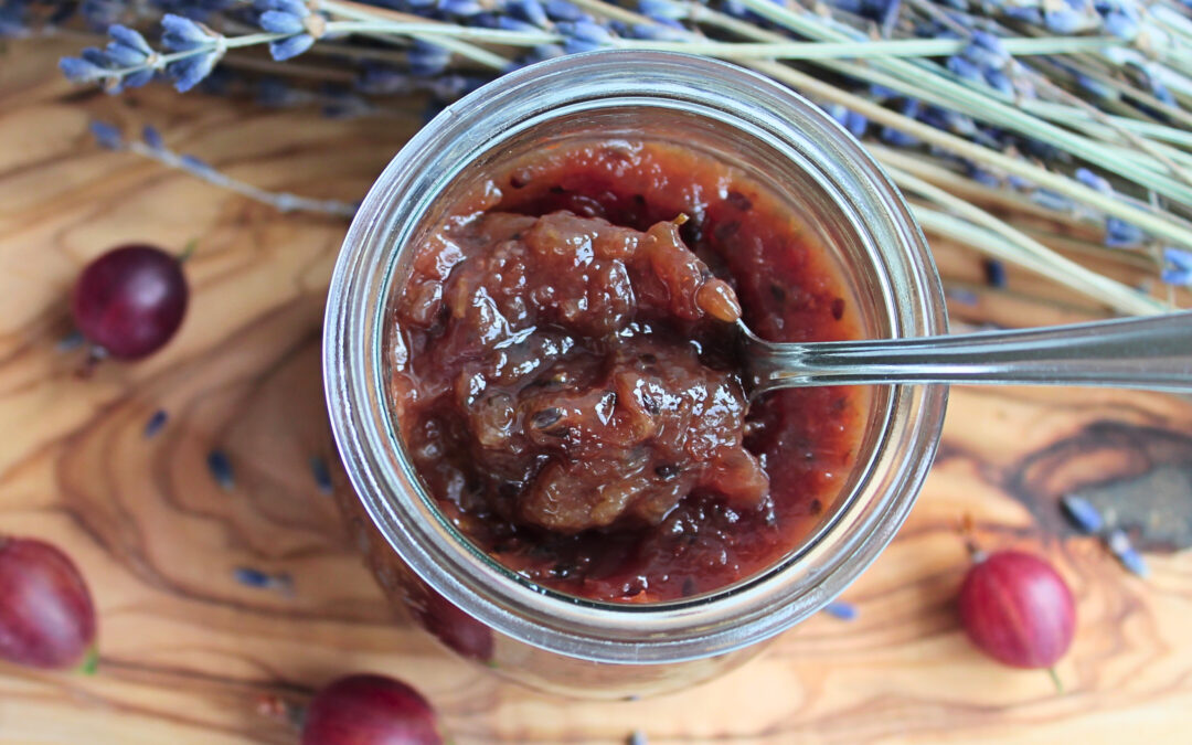 Stachelbeermarmelade mit Lavendel in einem Glas auf Holzbrett mit Lavendelblüten – von oben fotografiert