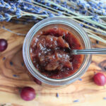 Stachelbeermarmelade mit Lavendel in einem Glas auf Holzbrett mit Lavendelblüten – von oben fotografiert