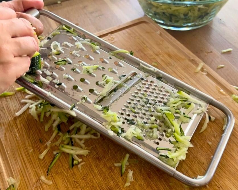 zucchini-raspeln-fuer-das-trocknen.jpg Frische Zucchini werden auf einer Reibe grob geraspelt – perfekt für spätere Verwendung als Zucchinimehl oder für Gemüsebratlinge.