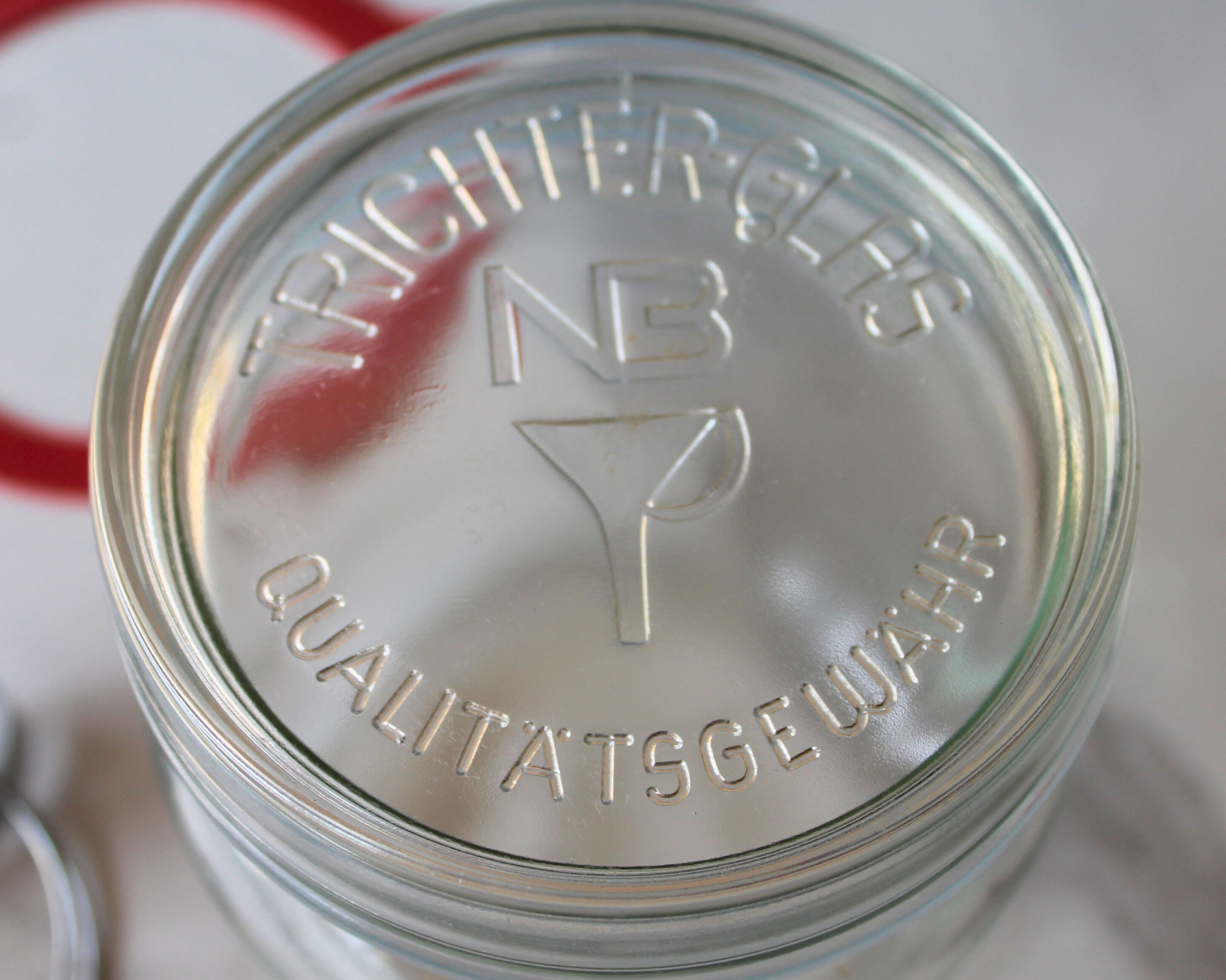 Glasdeckel eines NB Trichterglases mit geprägtem Schriftzug „Qualitätsgewähr“.