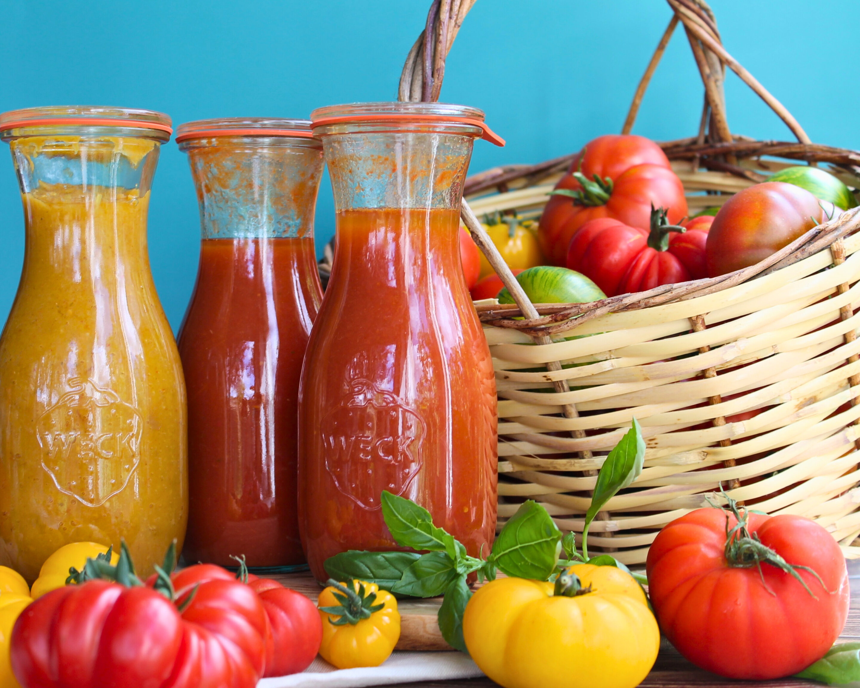 tomatensauce-einkochen-weckflaschen-gemuesekorb.jpg Drei Weckflaschen mit eingekochter Tomatensauce neben einem Korb voller frischer Tomaten und Basilikum.