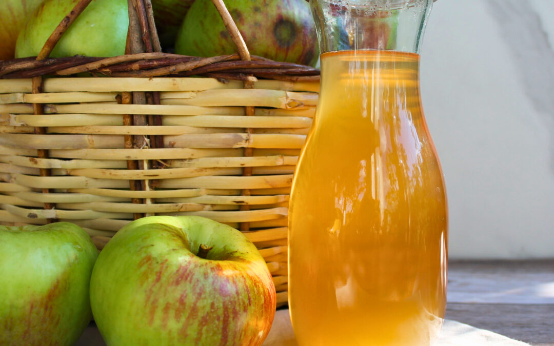 Apfelsaft einkochen: Karaffe mit klarem Apfelsaft neben einem Korb voller Äpfel.
