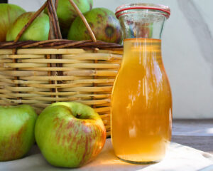Apfelsaft einkochen: Karaffe mit klarem Apfelsaft neben einem Korb voller Äpfel.