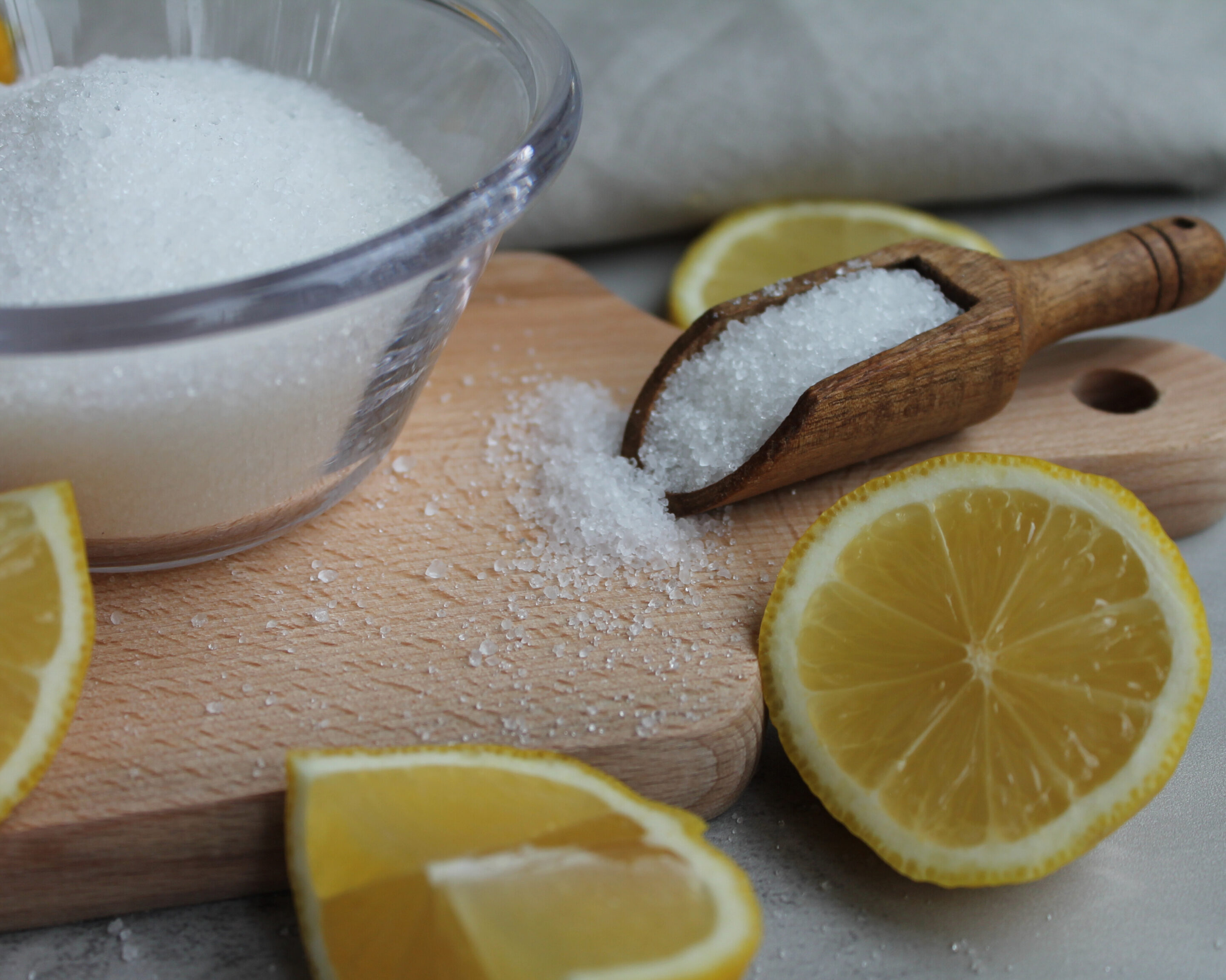 Schale und Holzschaufel mit Salz auf einem Schneidebrett, umgeben von frischen Zitronenscheiben – fotografiert für Beiträge zu Säuregehalt, Salz und sicheres Fermentieren.