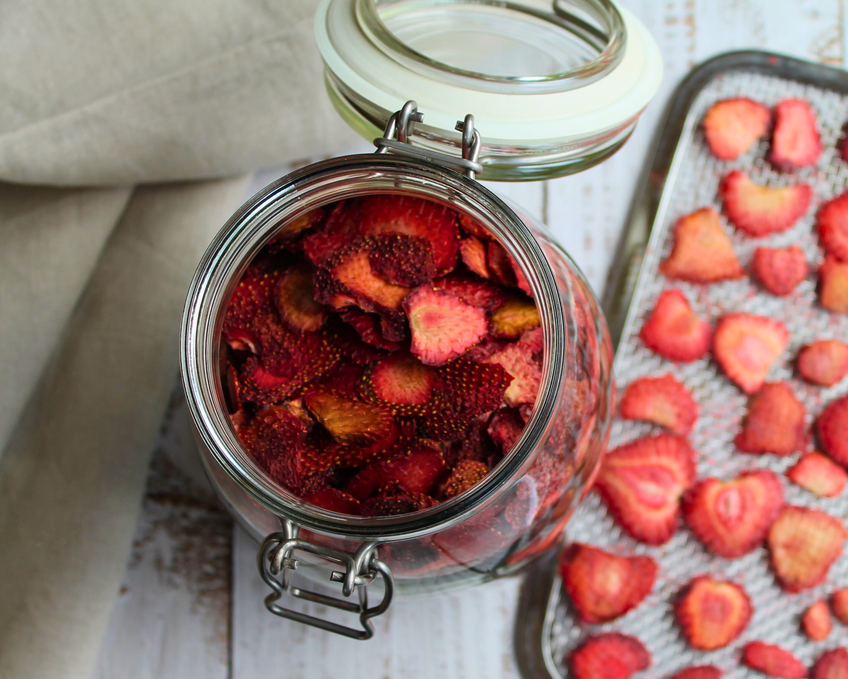 Ein Glas mit getrockneten Erdbeerscheiben, daneben ein Dörrblech – fruchtige Geschenkidee aus der Vorratskammer.