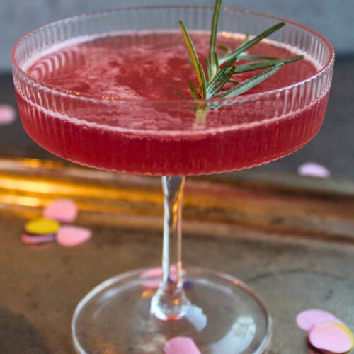 Winter-Berry Fizz mit Rosmarin in einer Sektschale, Cocktail aus Beerenmarmelade und Sekt