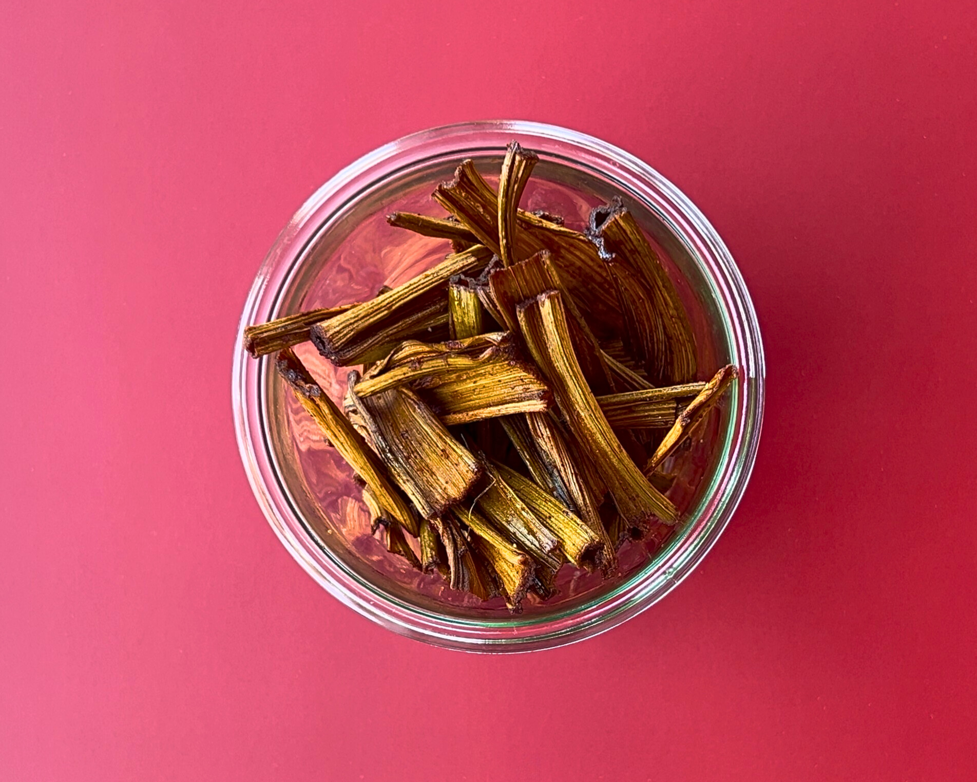 Glas mit getrockneten Rhabarberstreifen auf rotem Hintergrund – Rhabarber-Jerky als kreative Geschenkidee aus der Vorratskammer.