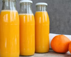 Drei Flaschen mit selbst eingekochtem Orangensaft ohne Zusatzstoffe, im Wasserbad haltbar gemacht – frischer Orangensaft im Glas als Vorrat für den Winter.