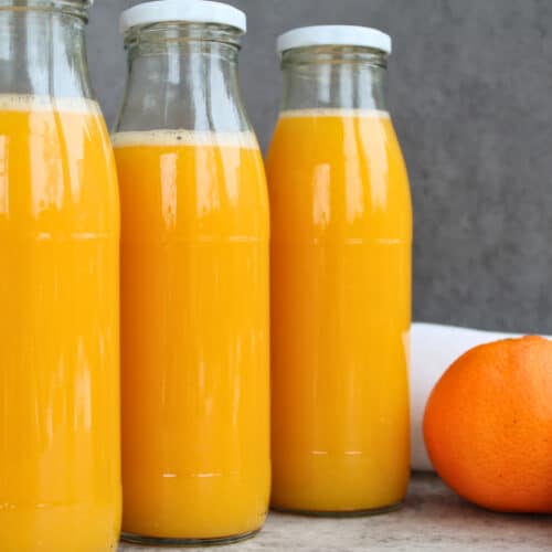 Drei Flaschen mit selbst eingekochtem Orangensaft ohne Zusatzstoffe, im Wasserbad haltbar gemacht – frischer Orangensaft im Glas als Vorrat für den Winter.
