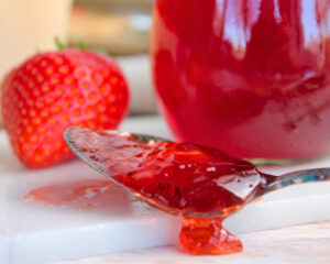 Löffel mit festem Erdbeer-Gelee über einem Marmeladenglas – die Konsistenz zeigt den erreichten Gelierpunkt.