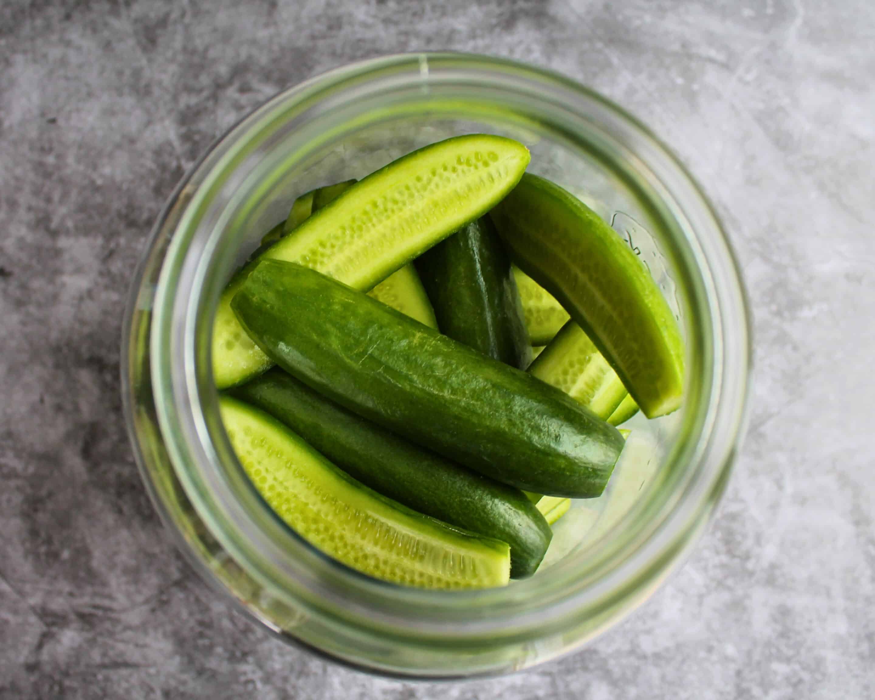 Gurkenstücke mit Gewürzen in ein Glas zum Fermentieren geschichtet