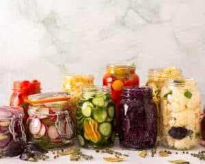 Verschiedene fermentierte Gemüsesorten in Gläsern wie Gurken, Karotten, Kohl und Radieschen