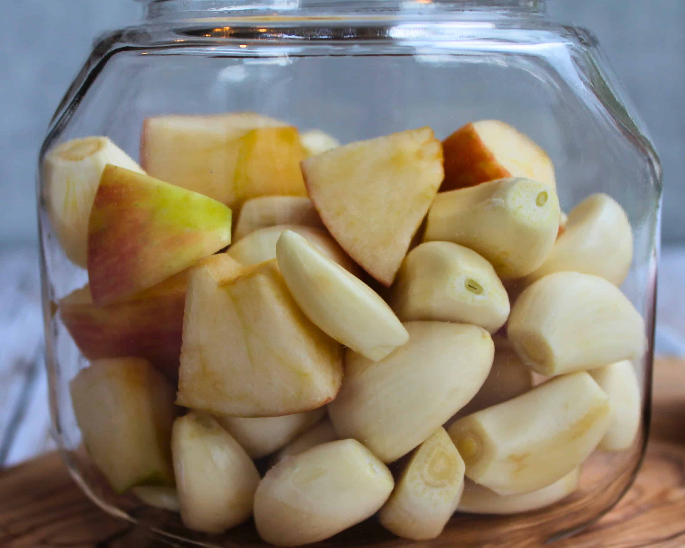 Geschälter Knoblauch und Apfelstücke im Glas vor der Fermentation in Salzlake