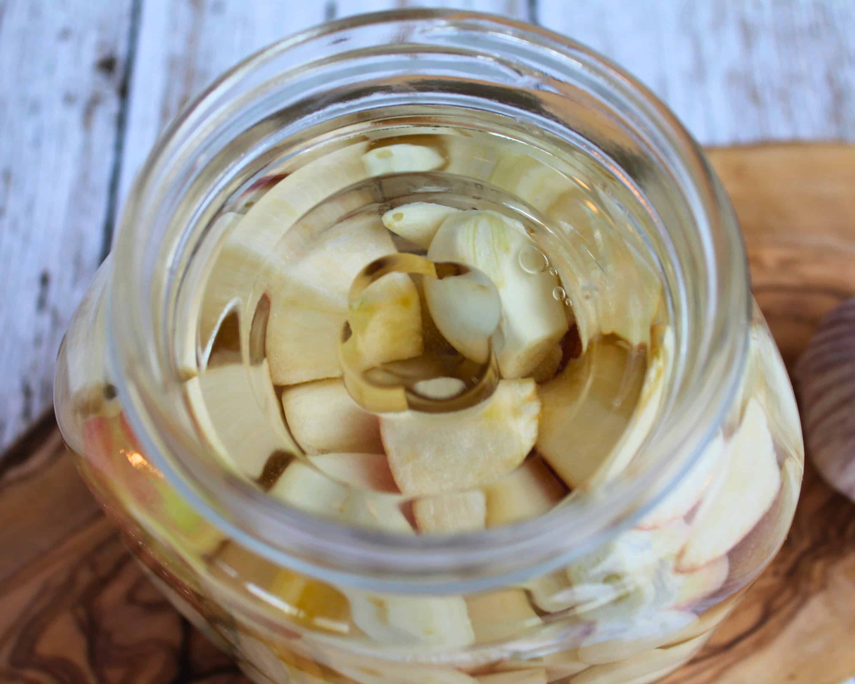 Knoblauch und Apfelstücke im Glas vollständig mit Salzlake bedeckt für die Fermentation