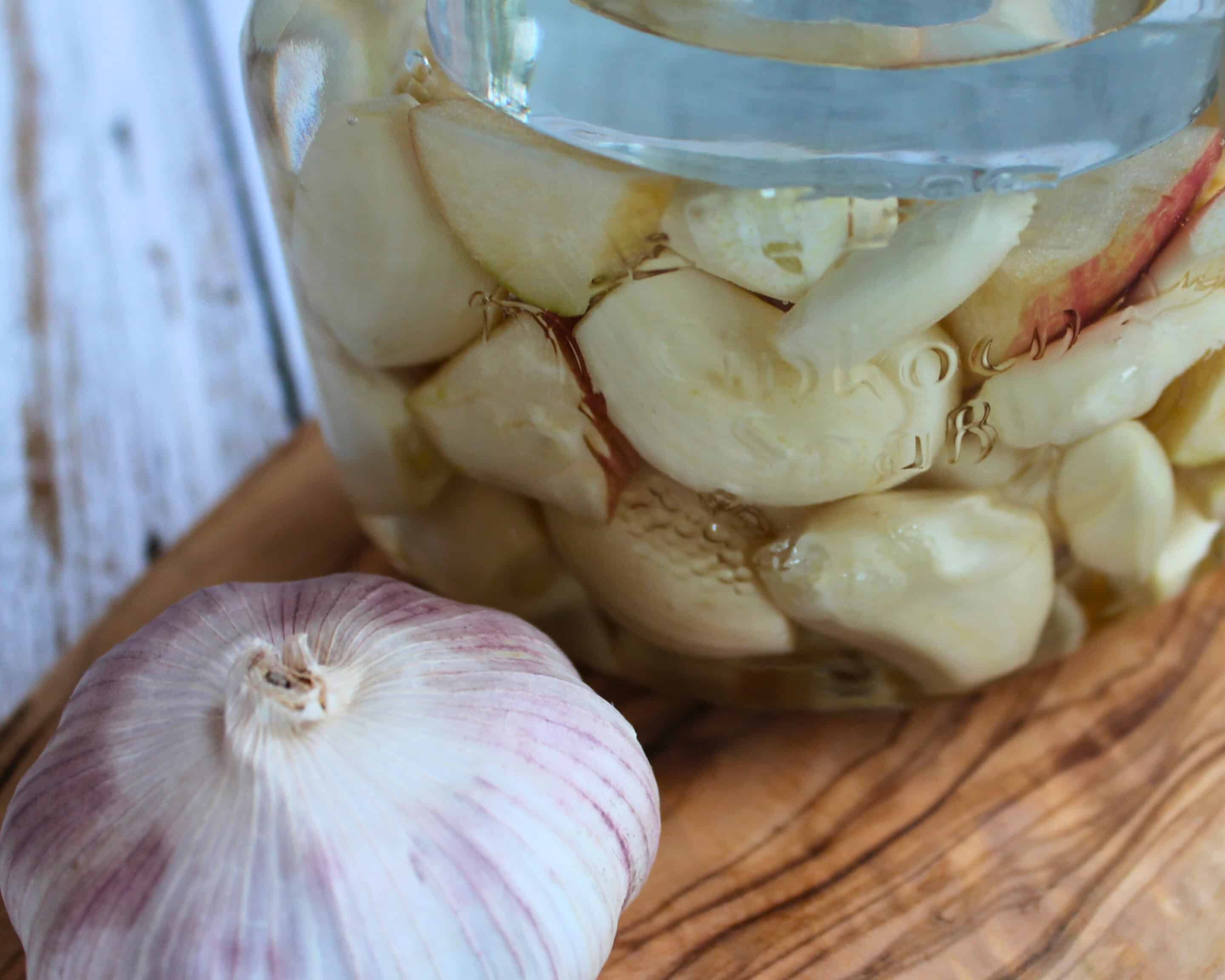 Knoblauch in Salzlake im Glas mit ganzer Knoblauchknolle daneben