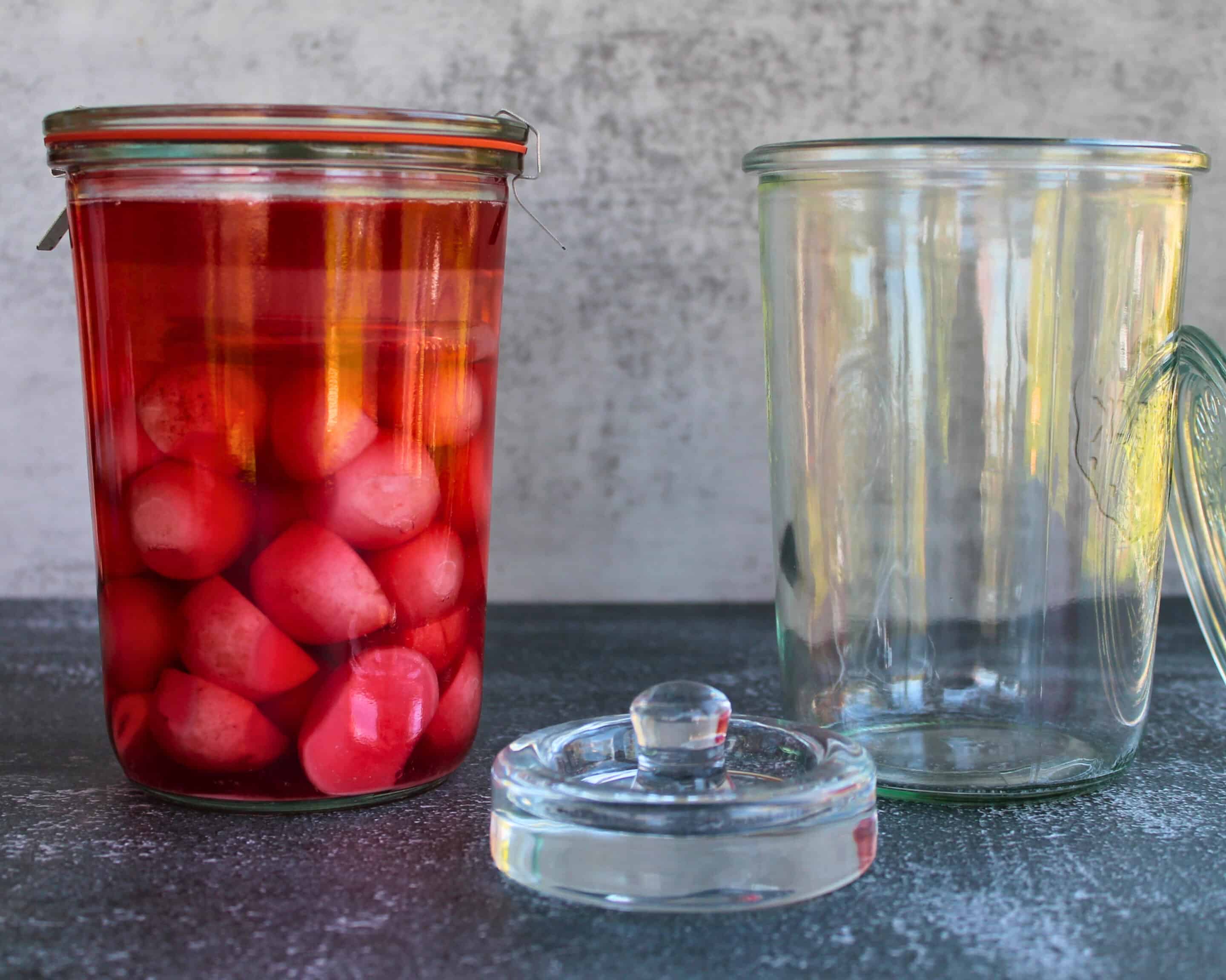 Ein gefülltes Weckglas mit fermentierten Radieschen neben einem leeren, sauberen Glas – Vorbereitung und Ergebnis im Vergleich
