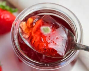 Löffel mit Erdbeermarmelade über geöffnetem Glas, auf der Marmelade ist ein kleiner Schimmelfleck sichtbar.