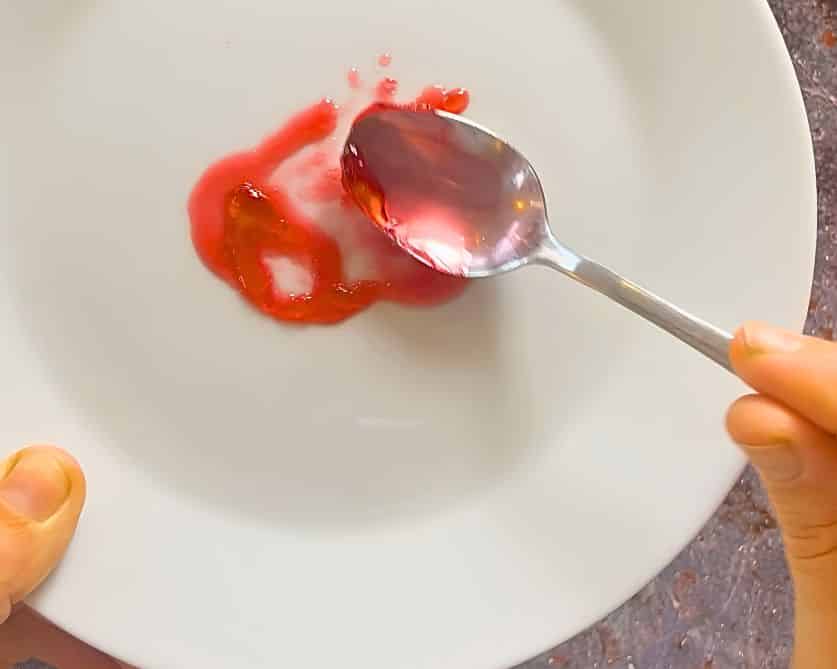 Gelierprobe von Erdbeermarmelade auf einem weißen Teller. Die Marmelade wirkt noch flüssig und läuft auseinander.