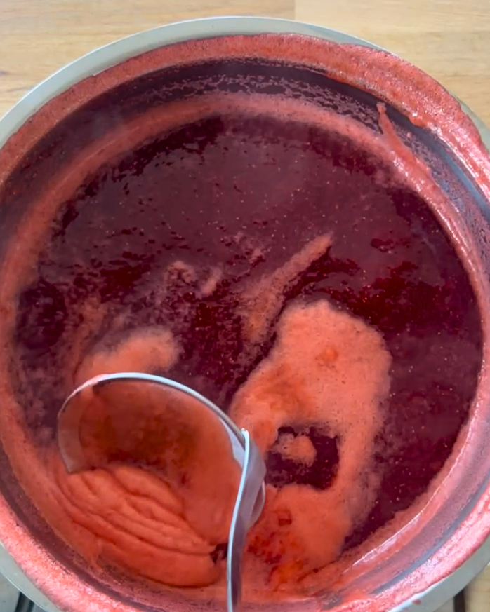 Schöpflöffel schöpft Schaum aus kochender Erdbeermarmelade in einem Topf