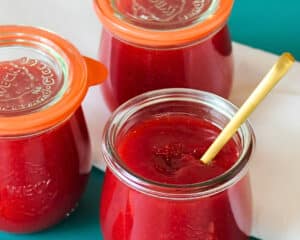 Drei Gläser Erdbeermarmelade mit Gelierprobe und Löffel. Das Bild zeigt eine selbstgemachte Erdbeermarmelade mit kräftiger roter Farbe und fester Konsistenz.
