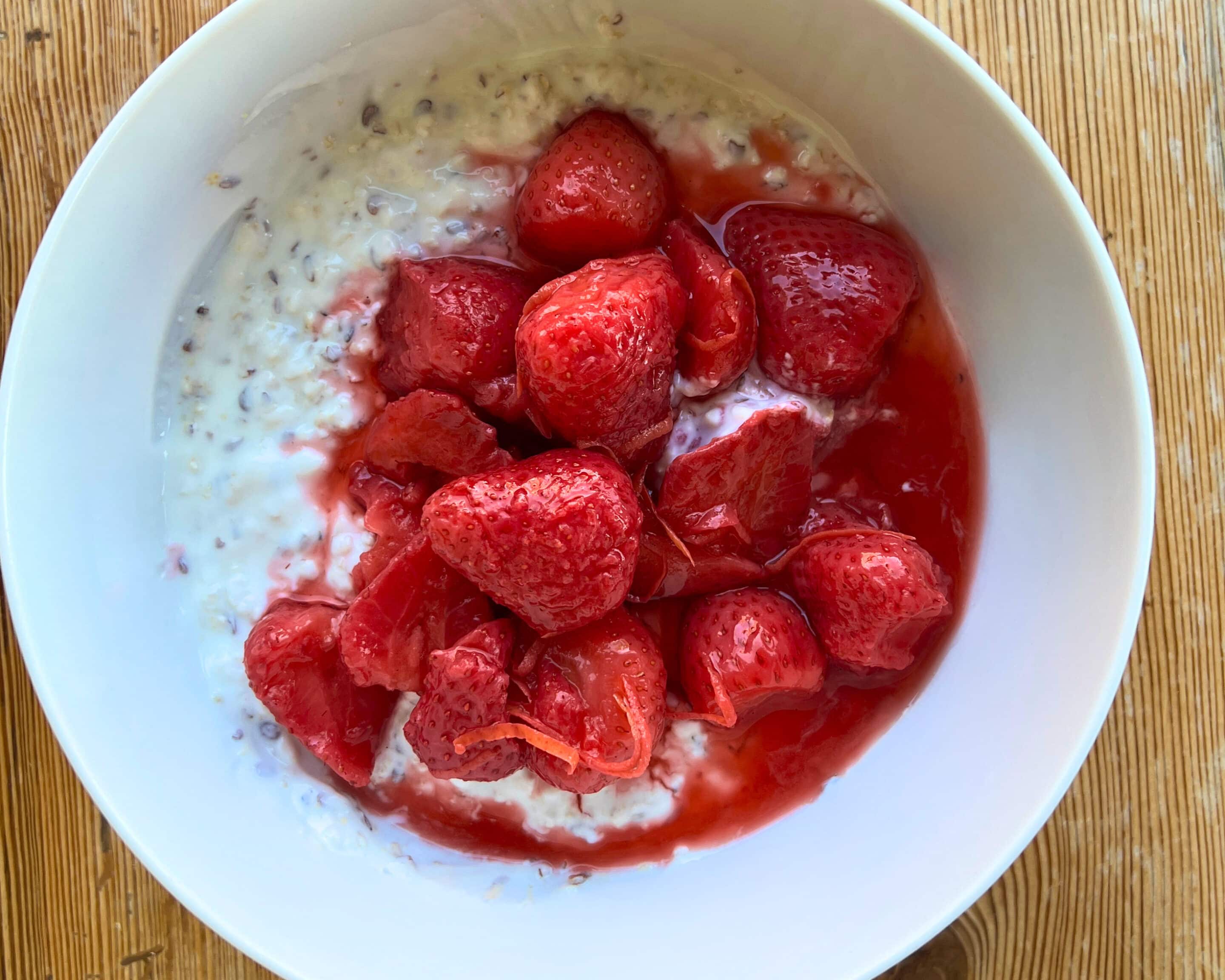 Fermentierte Erdbeeren mit rotem Fruchtsaft über Haferflocken und Joghurt in einer weißen Schüssel