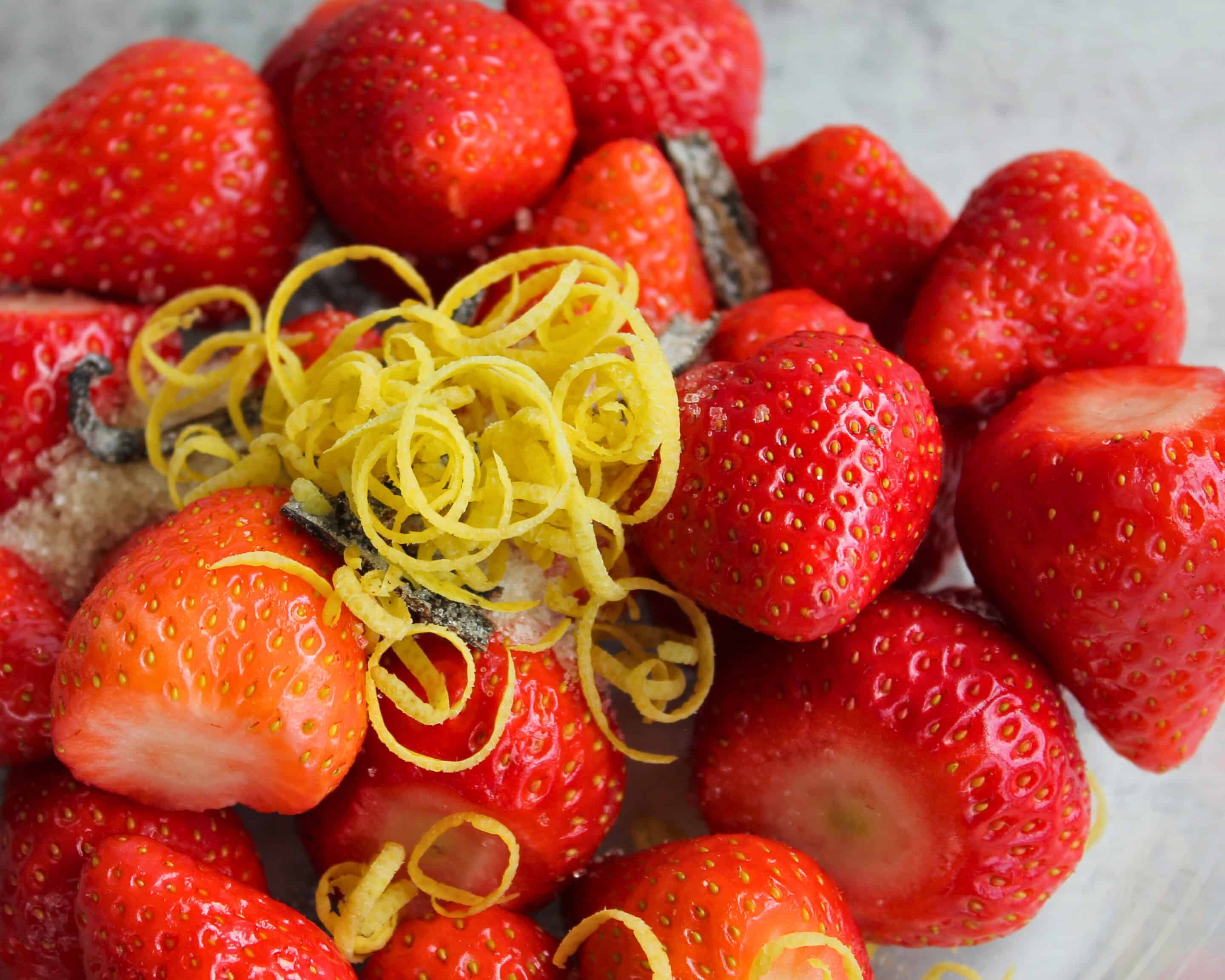Frische Erdbeeren mit Zucker, Salz und Zitronenschale in einer Glasschüssel vor der Fermentation