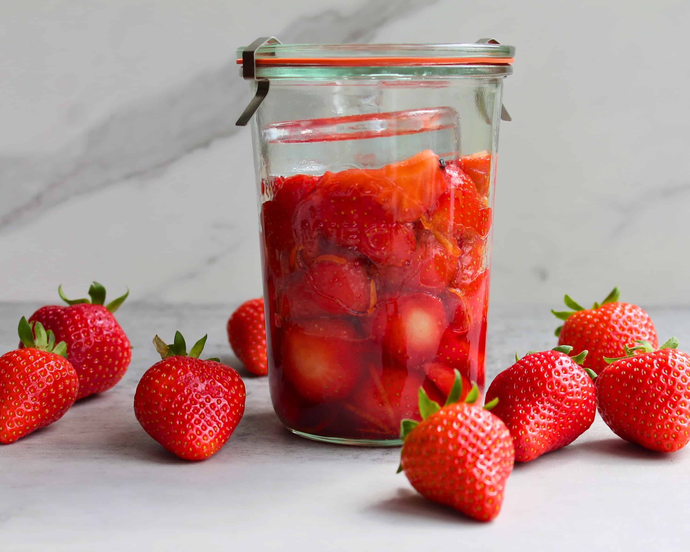 Frisch eingelegte Erdbeeren in einem Weckglas umgeben von frischen Erdbeeren
