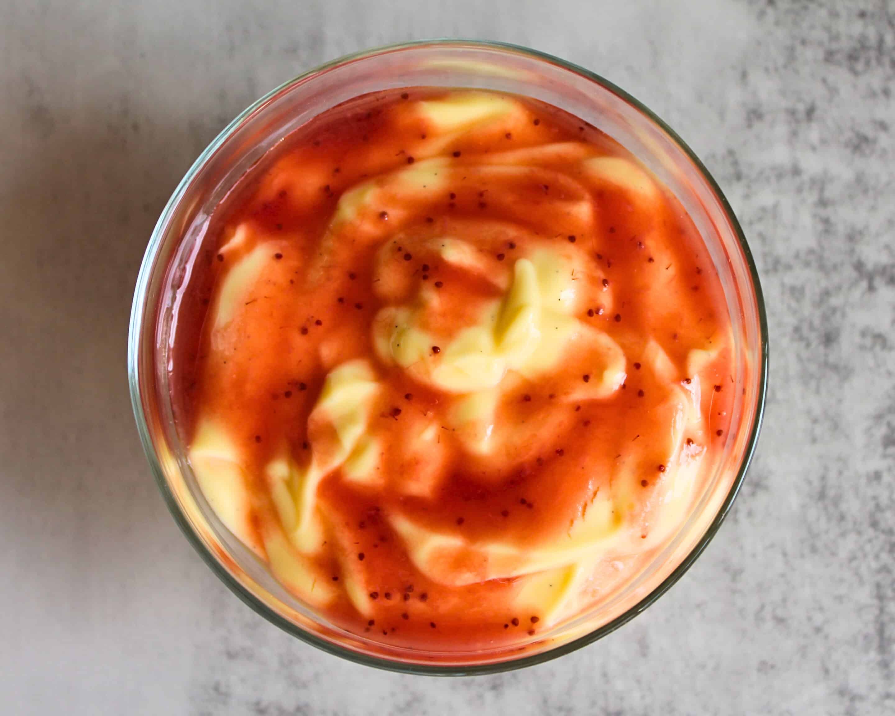 Erdbeerpüree auf Joghurt in einem Glasbecher von oben – fruchtige Sauce als Dessert-Topping