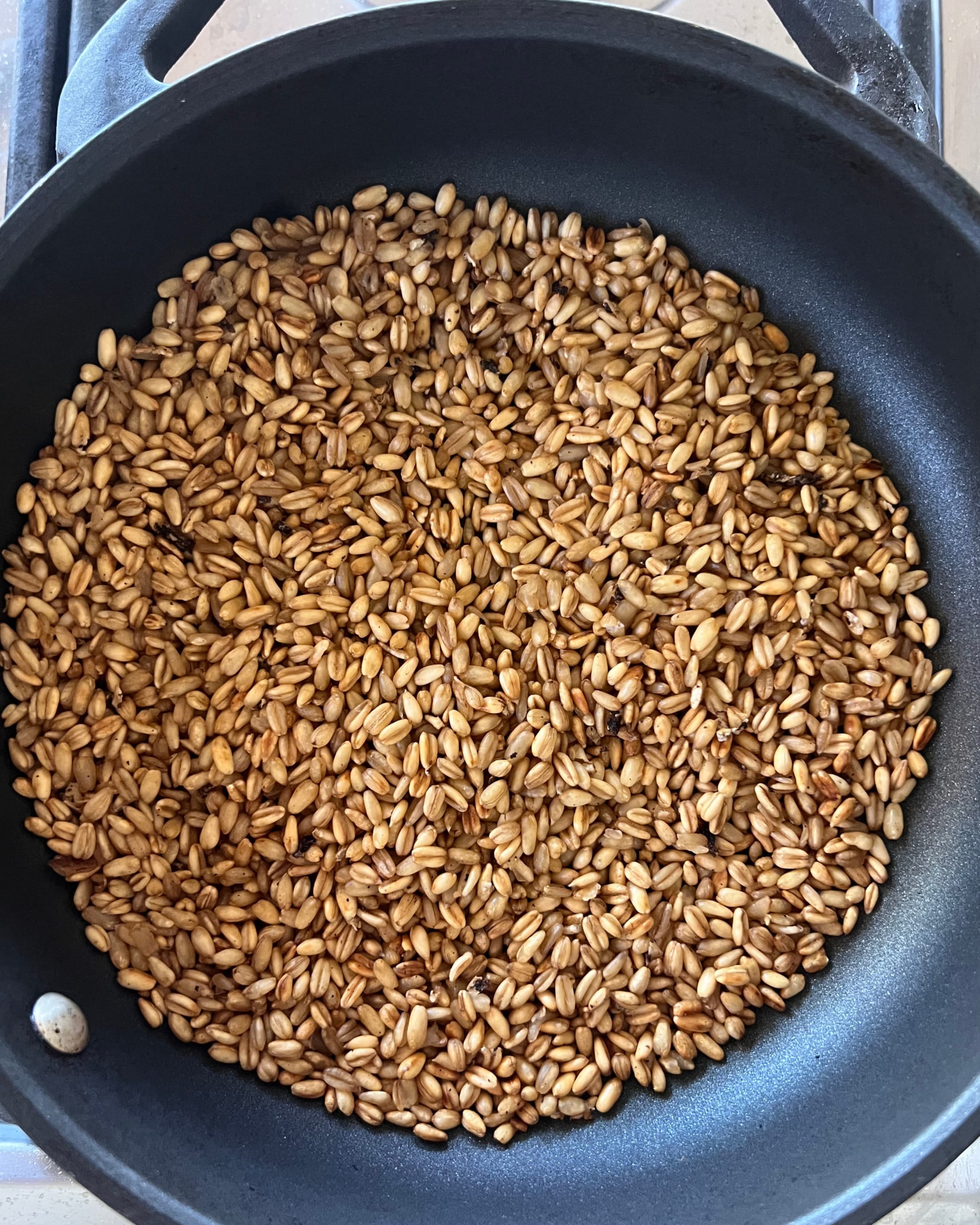 Fermentierter Hafer während des Röstens mit erster goldbrauner Färbung in der Pfanne.