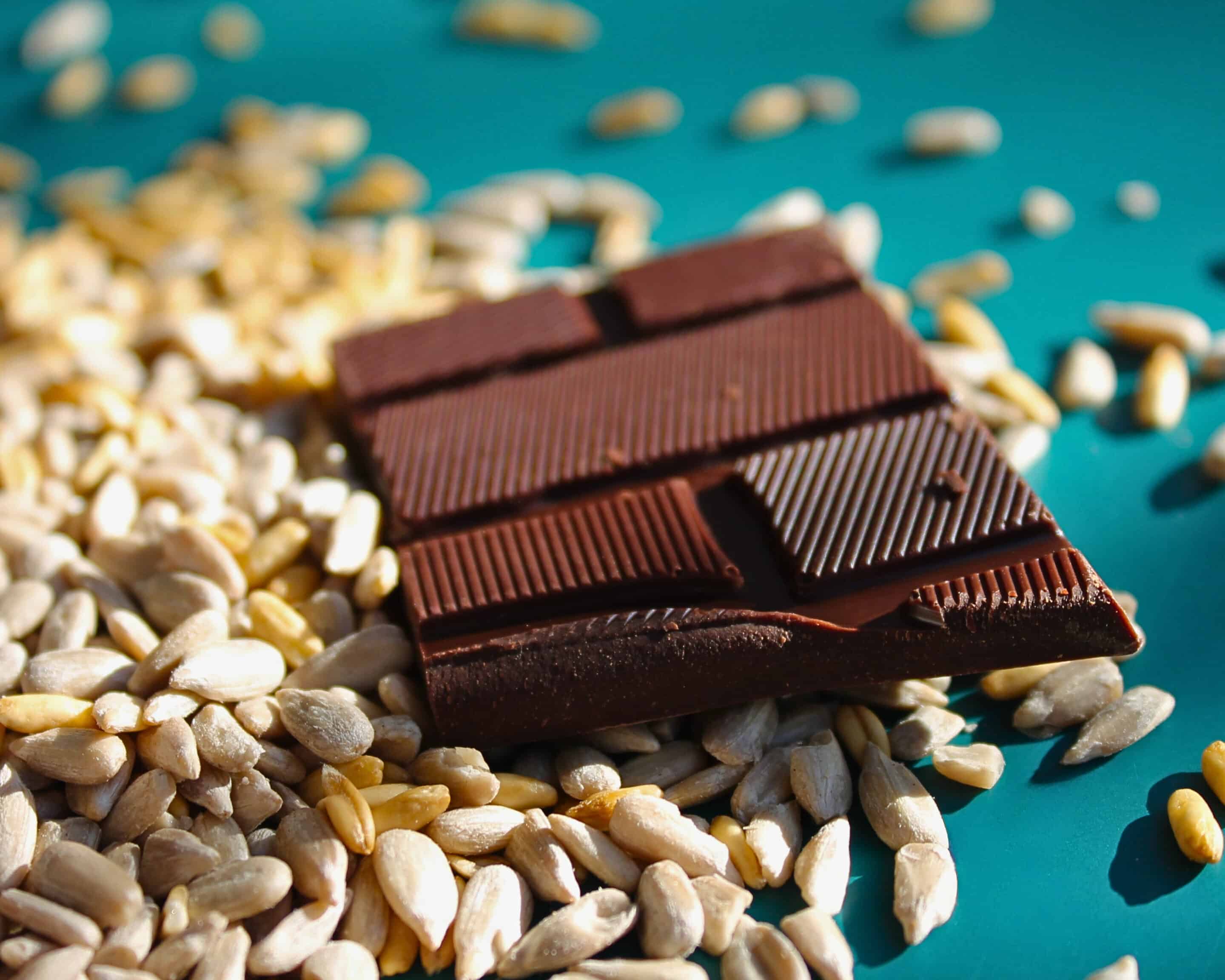 Stück dunkler Schokolade auf geschälten Sonnenblumenkernen als Vergleich zum selbstgemachten Schokoladenersatz aus fermentierten Sonnenblumenkernen.