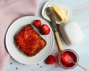 Scheibe Vollkornbrot mit glänzendem Erdbeergelee, serviert mit frischen Erdbeeren und einem Glas Gelee.