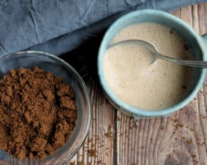 Gemahlener Schokoladenersatz aus fermentierten Sonnenblumenkernen neben einer Tasse des fertigen Getränks.