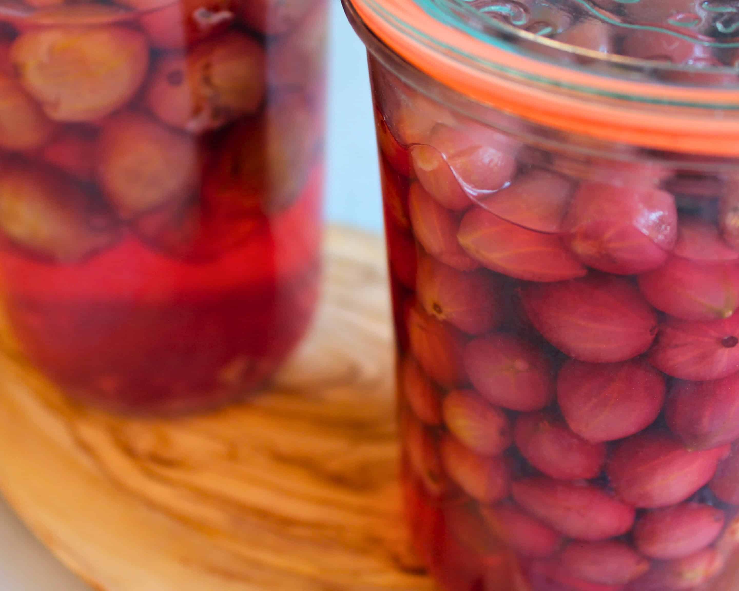 Nahaufnahme eines prall mit Stachelbeeren gefüllten Weckglases im rötlichen Aufguss