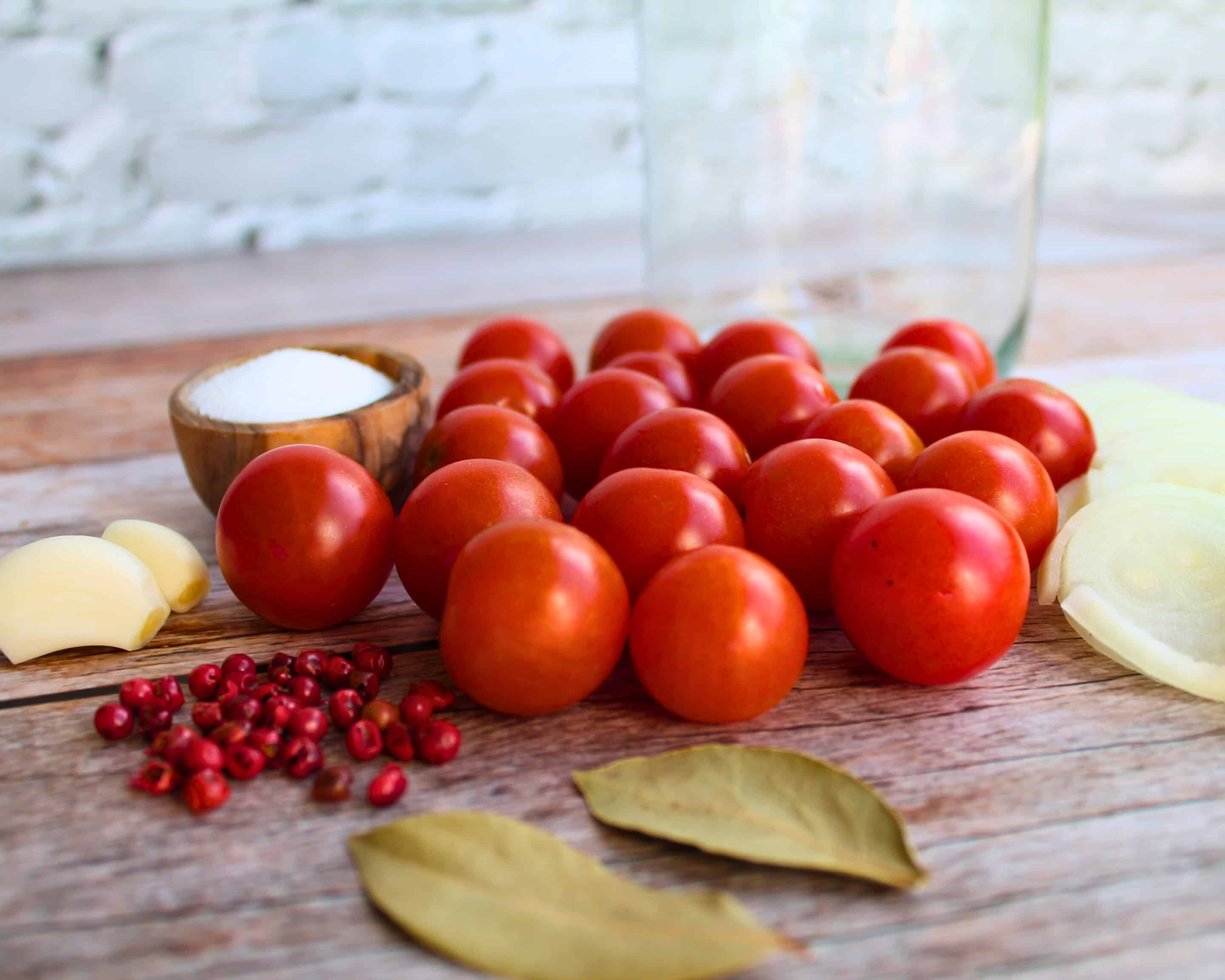Zutaten zum Tomaten fermentieren auf Holzbrett: Cocktailtomaten, Salz, Knoblauch, Zwiebel, rosa Pfefferbeeren und Lorbeerblätter